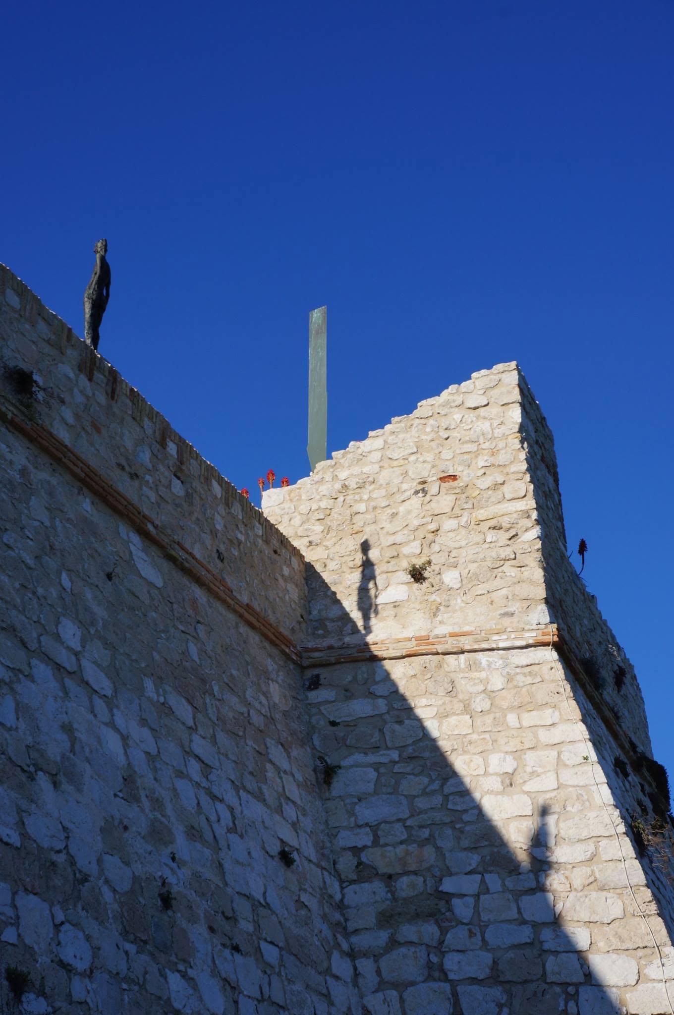 Ramparts and a statue against a deep blue Riviera sky